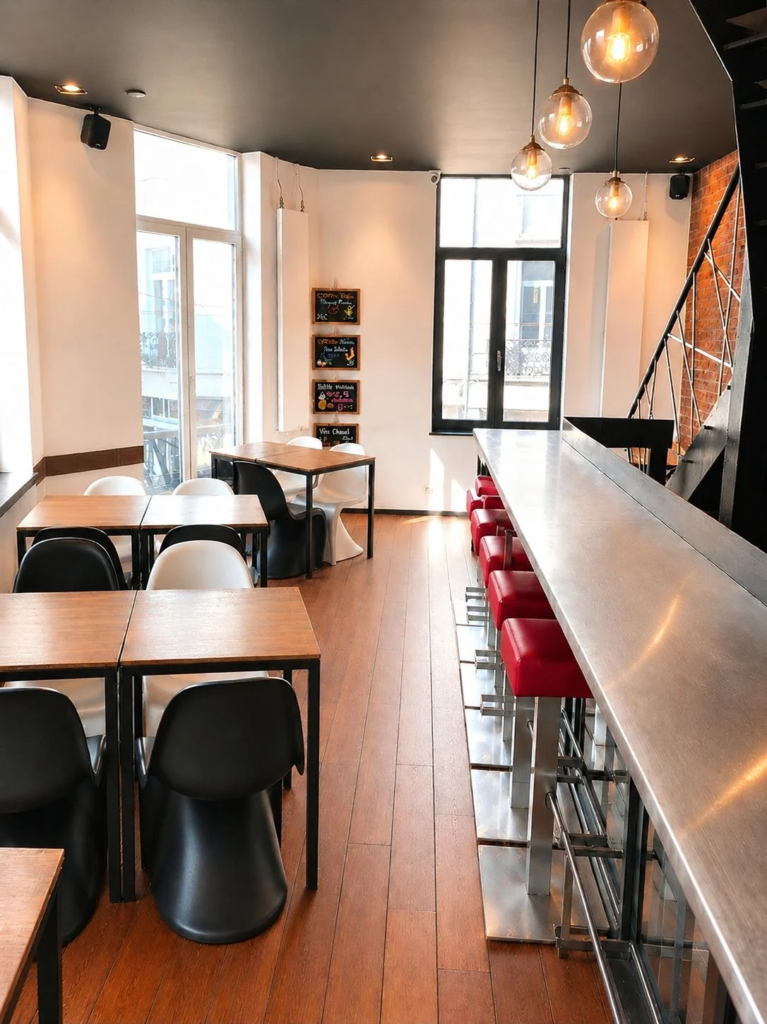 Salle du ROXI avec bar en inox, tabourets en cuir rouge et entrée vitrée sur la rue
