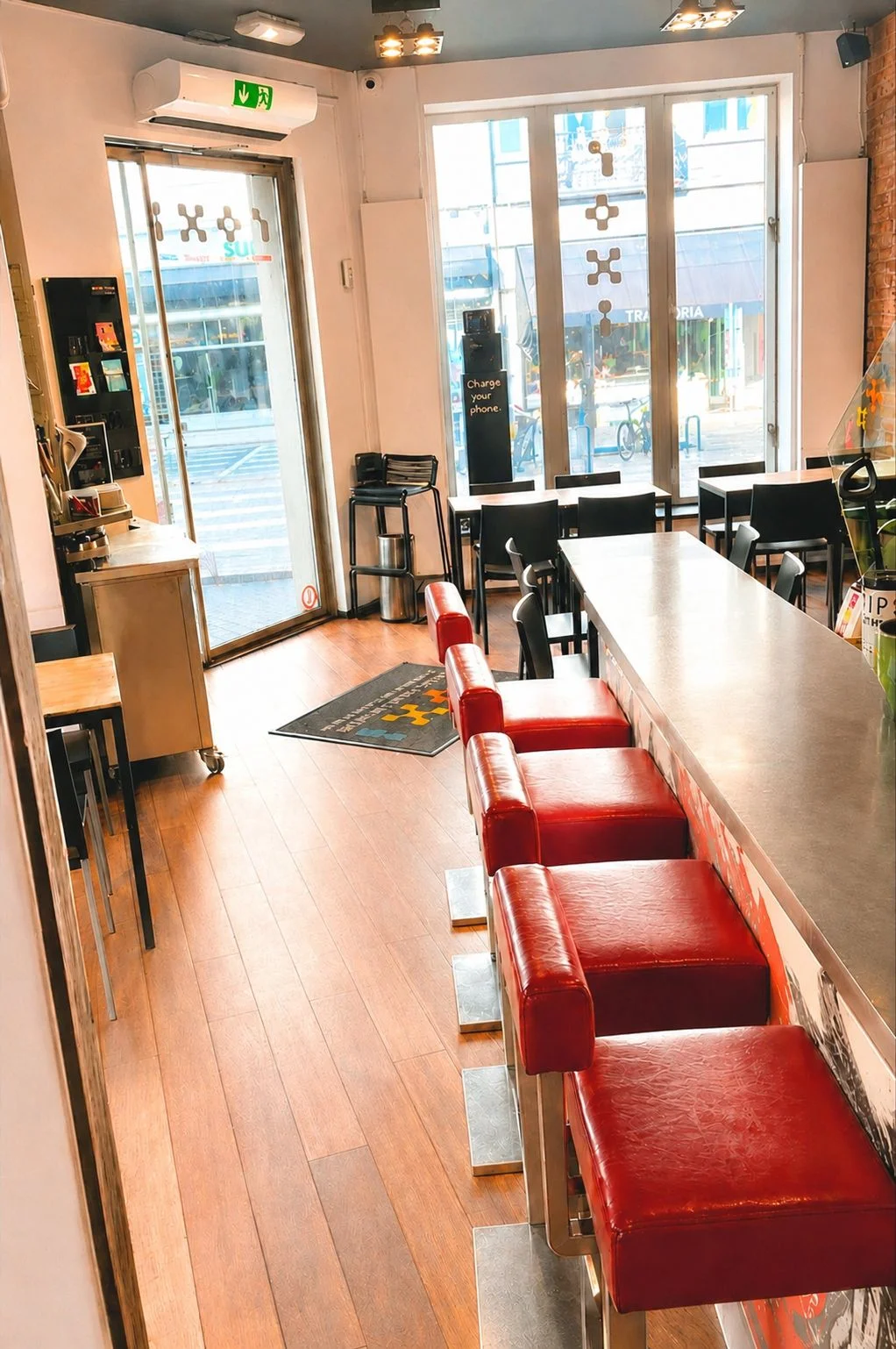 Bar du ROXI avec tabourets rouges, mur de bouteilles et grandes baies vitrées sur la rue du Bailli